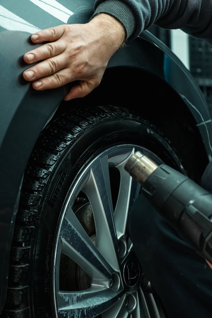 Home Hands working on a car tire using a heat gun, showing automotive maintenance in a workshop setting.
